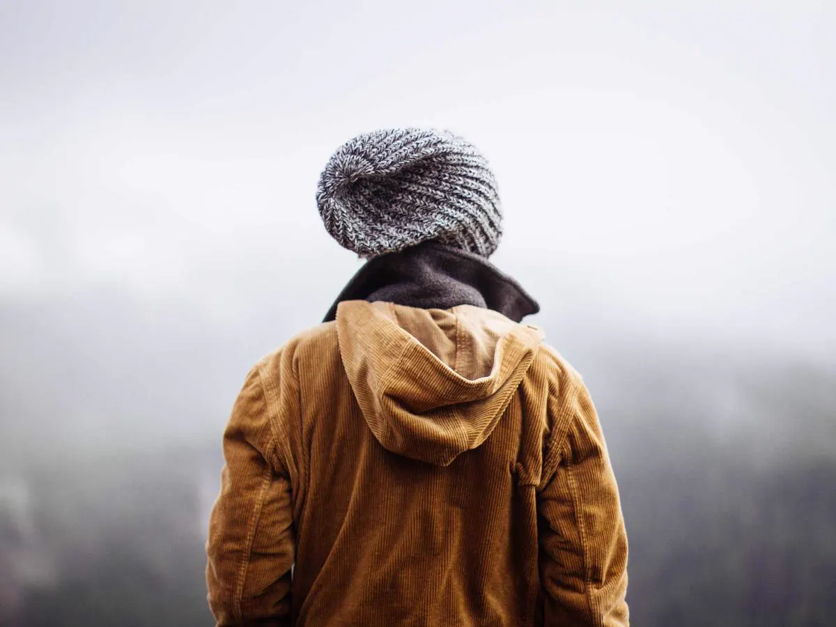 Pessoa de casaco amarelo e gorro caminhando na neblina